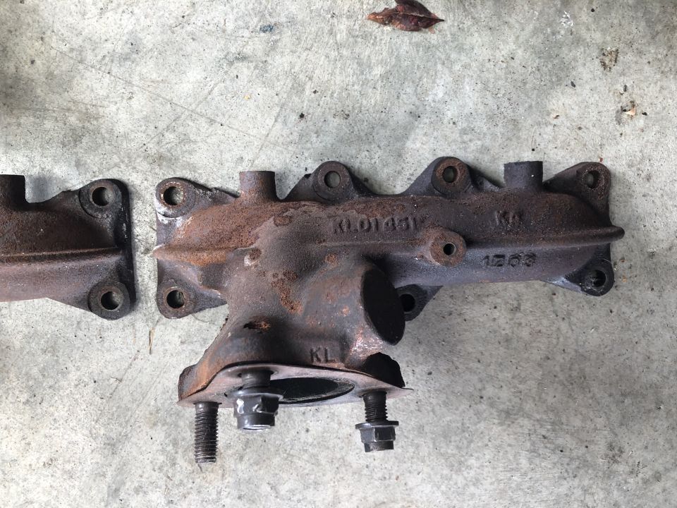 Two rusty exhaust manifold sections with part numbers visible
