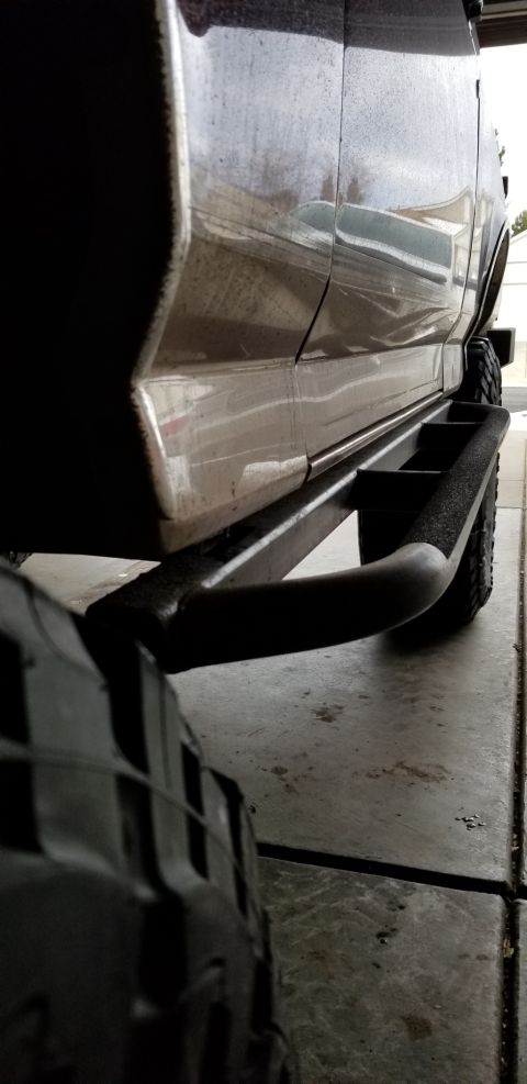 1996 Ford Bronco - Side view of a dark SUV aftermarket tubular side steps and large tires.