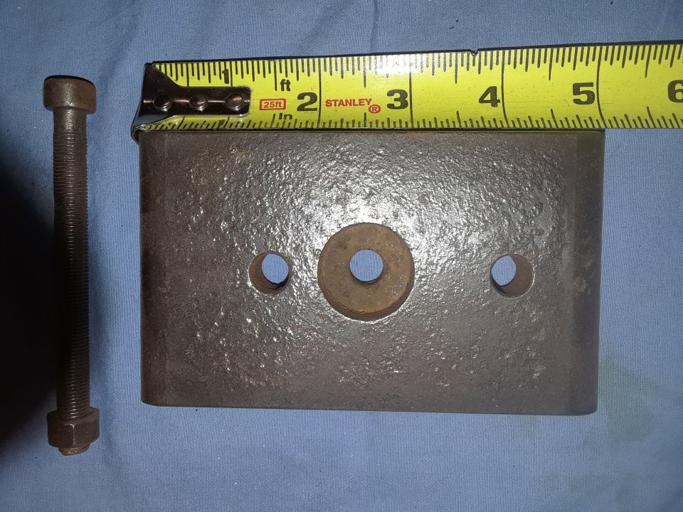 Metal plate with holes and a bolt next to a measuring tape.