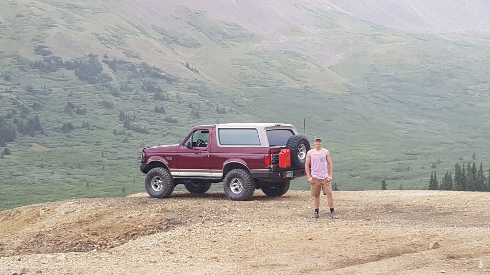 Maroon 1996 Ford Bronco parked on a mountain road with a man standing beside it.