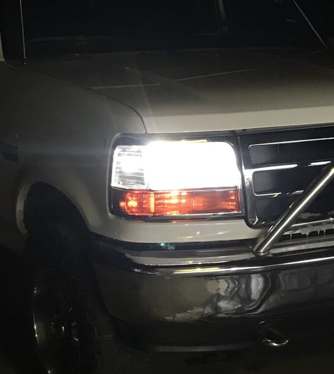 1995 Ford Bronco - The front right headlight and turn signal of a white Ford Bronco are illuminated. The vehicle has a chrome bumper and a black grille.