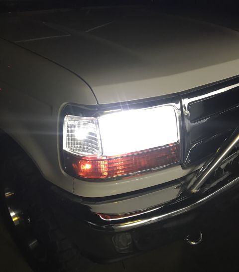 1995 Ford Bronco - The front passenger side headlight of a white Ford Bronco is illuminated, showing the clear lens and amber turn signal. The vehicle has a c…