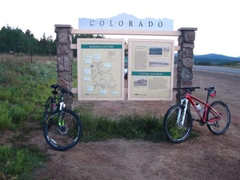 1996 Ford Bronco - Two mountain bikes are parked in front of a welcome sign for Colorado. The sign has two informational panels and the word "COLORADO" across…