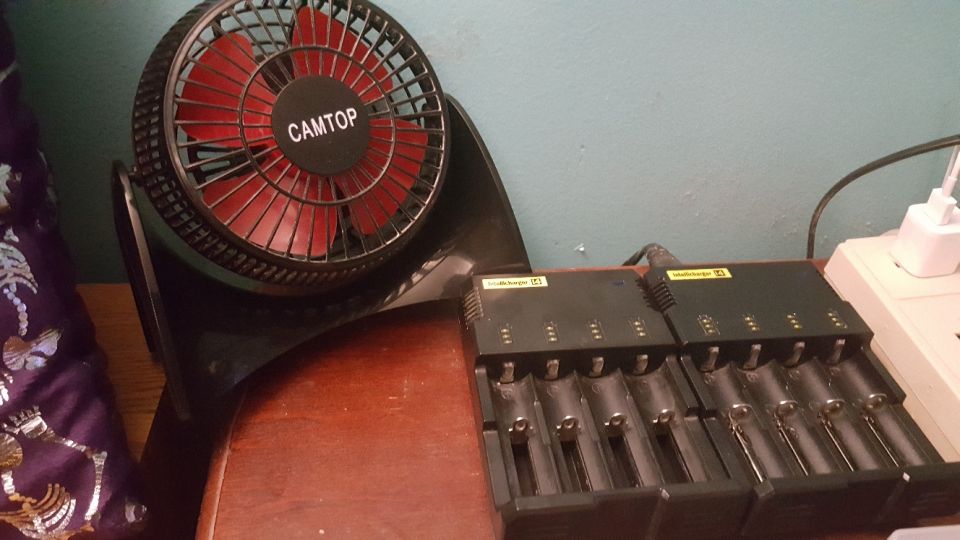 Black desk fan with red blades and "CAMTOP" text next to a battery charger.