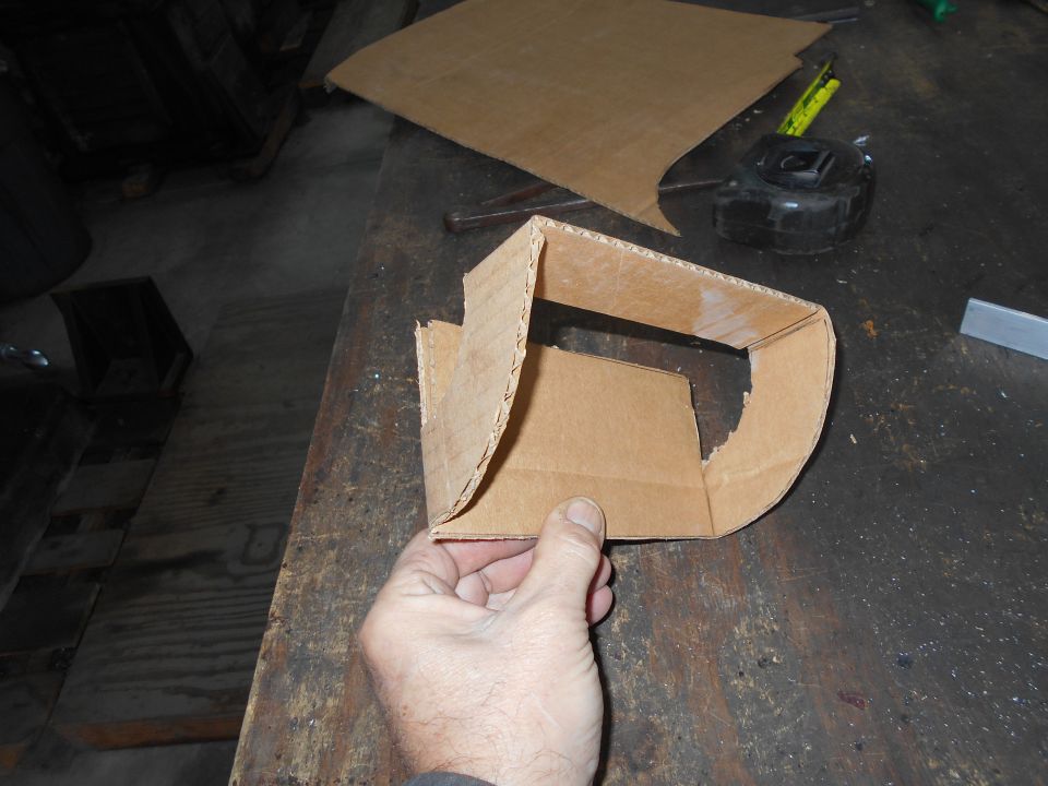 Hand holding a cardboard bracket with a tape measure and cardboard pieces on a workbench.