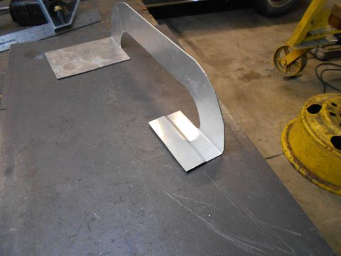 1992 Ford Bronco - A close-up view of metal fabrication in progress, showing bent and cut aluminum pieces on a dark metal surface. A yellow wheel rim and part…