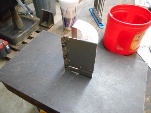 1992 Ford Bronco - A metal bracket with a curved top sits on a dark grey surface. To the right is a red plastic bucket and a set of hex wrenches.
