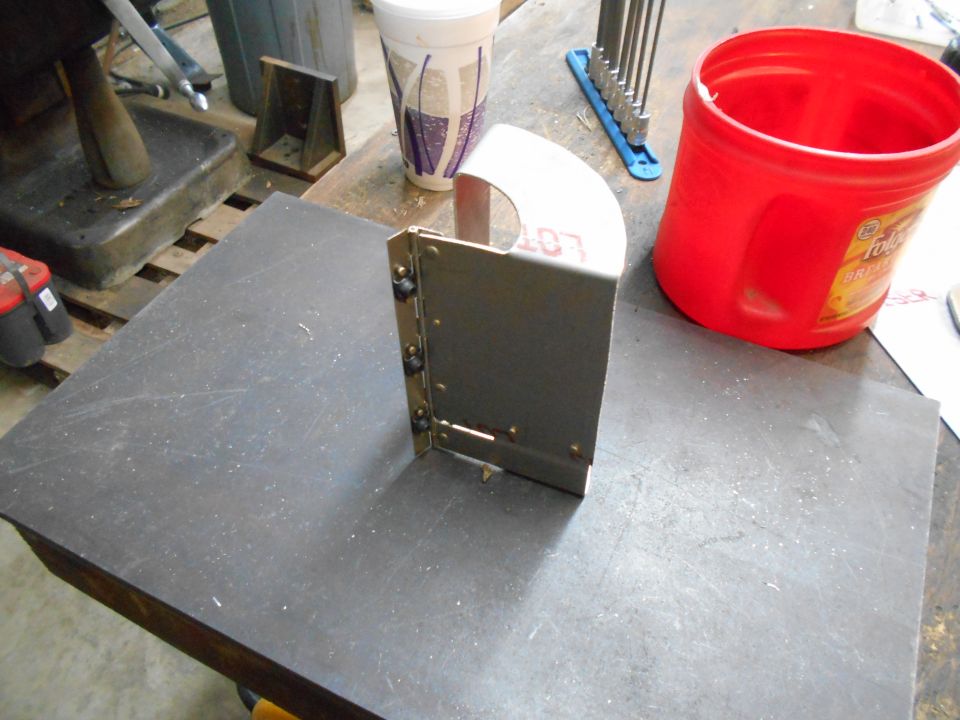 Metal bracket with curved top, red bucket, and hex wrenches on a workbench.