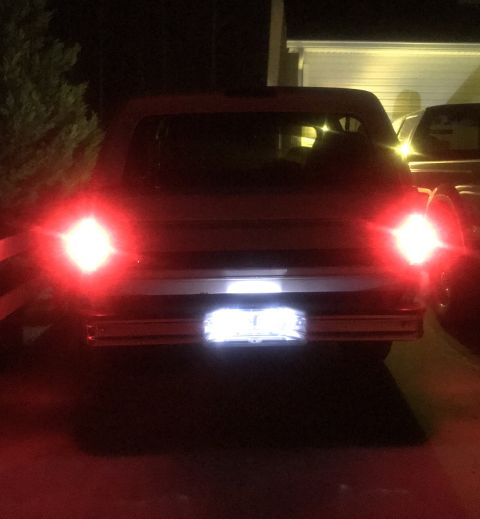 1995 Ford Bronco - The rear of a red SUV with its brake lights illuminated at night. The license plate light is also on, illuminating a license plate.
