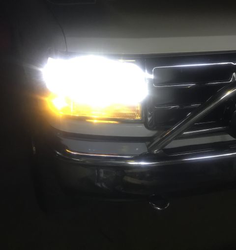 1995 Ford Bronco - The front of a white Ford truck with its headlights on. The chrome grille and bumper are visible, along with a portion of a chrome bull bar.