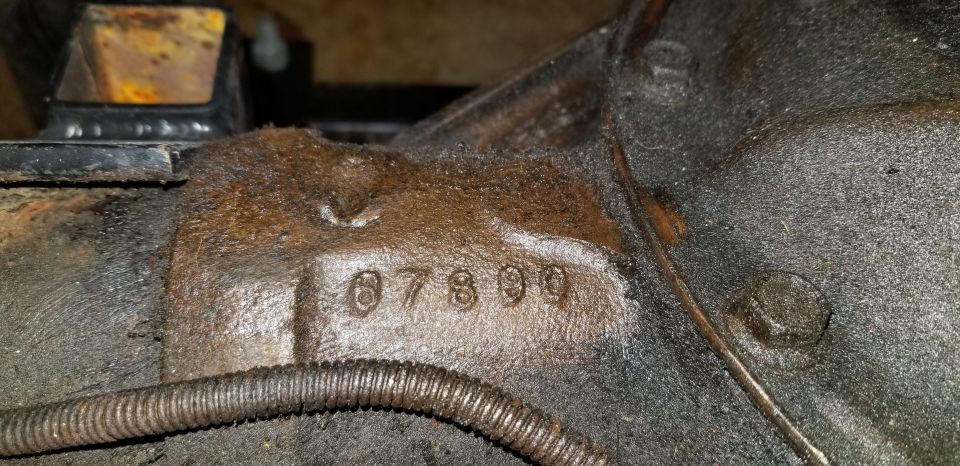Stamped numbers 07899 on a greasy automotive part with metal conduit.