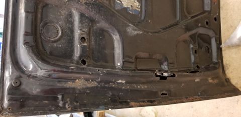 1970 Pontiac GTO — Underside of a black car hood with rust and latch mechanism.