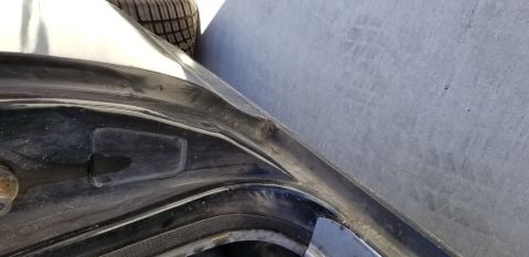 1970 Pontiac GTO — Close-up of dented black car body panel edge with tire in background.