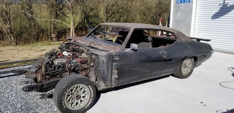 1970 Pontiac GTO coupe, black, partially disassembled, engine exposed, parked on concrete.
