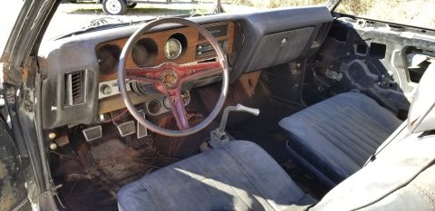 Interior view of a vintage Pontiac GTO with wood grain dash, red steering wheel, and blue seats.