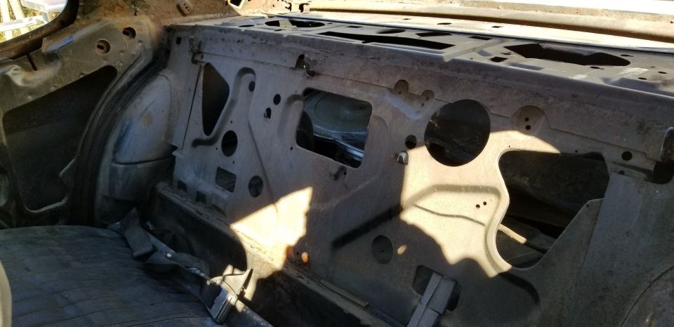 Interior of a classic car showing the rear firewall and seat area with sunlight and shadows.