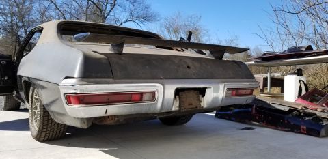 1970 Pontiac GTO - The rear view of a vintage, gray Pontiac GTO undergoing restoration. The car features a large rear spoiler, chrome bumper, and red tailligh…