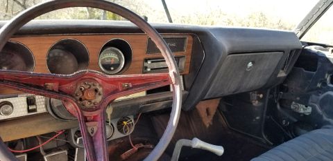 1970 Pontiac GTO - The interior of a vintage Pontiac GTO shows a red steering wheel, wood-grain dashboard accents, and various gauges. The dashboard is dusty,…