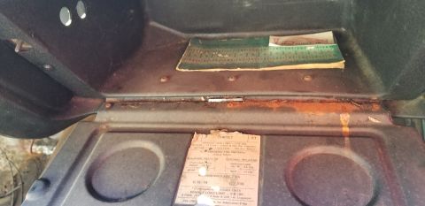 1970 Pontiac GTO - A close-up view inside a vehicle's glove compartment, showing a tire pressure sticker and some old documents. Rust is visible along the edg…
