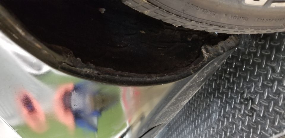 Close-up of rusted and damaged inner fender well of a black vehicle, with tire visible.