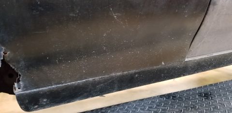 1970 Pontiac GTO - A close-up view of the lower body panel of a dark-colored vehicle, showing significant rust and damage on the left side. The panel appears…