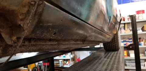 1970 Pontiac GTO - The underside of a vehicle's rocker panel and lower body is shown, lifted on a car lift. The metal shows signs of rust and minor dents, wit…