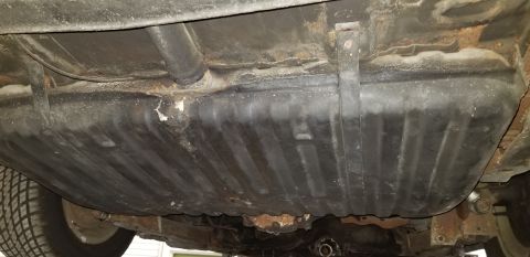 1970 Pontiac GTO - The underside of a vehicle shows a large, black fuel tank secured by metal straps. Rust is visible on the frame and surrounding components.