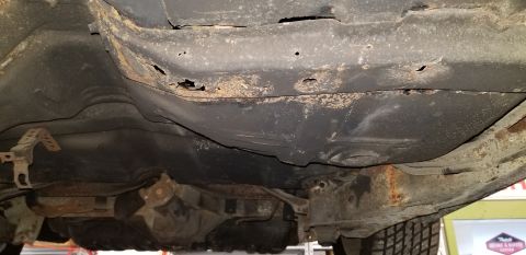 1970 Pontiac GTO - The underside of a vehicle shows significant rust and holes in the frame and body panels, indicating extensive corrosion. Various suspensio…