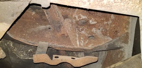 1970 Pontiac GTO - The underside of a vehicle shows significant rust on the frame and structural components. A bent metal bracket with two holes is visible in…
