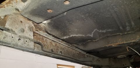 1970 Pontiac GTO - The underside of a vehicle shows significant rust on the frame rails and floor pan. A brake line is visible running along the frame.