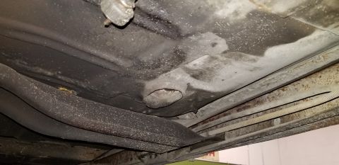 1970 Pontiac GTO - The underside of a vehicle shows a section of the frame and undercarriage with visible rust and grime. A circular opening is present in the…