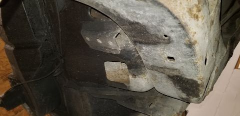 1970 Pontiac GTO - The underside of a vehicle's frame and wheel well shows significant rust and some black undercoating. A metal bracket with multiple bolt ho…