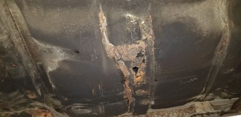 1970 Pontiac GTO - The undercarriage of a vehicle shows significant rust and holes in the metal frame. The dark undercoating is peeling away in areas, reveali…