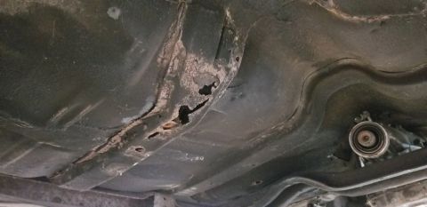 1970 Pontiac GTO - The underside of a vehicle shows significant rust and holes in the frame and floor pan. A portion of the transmission is visible on the rig…