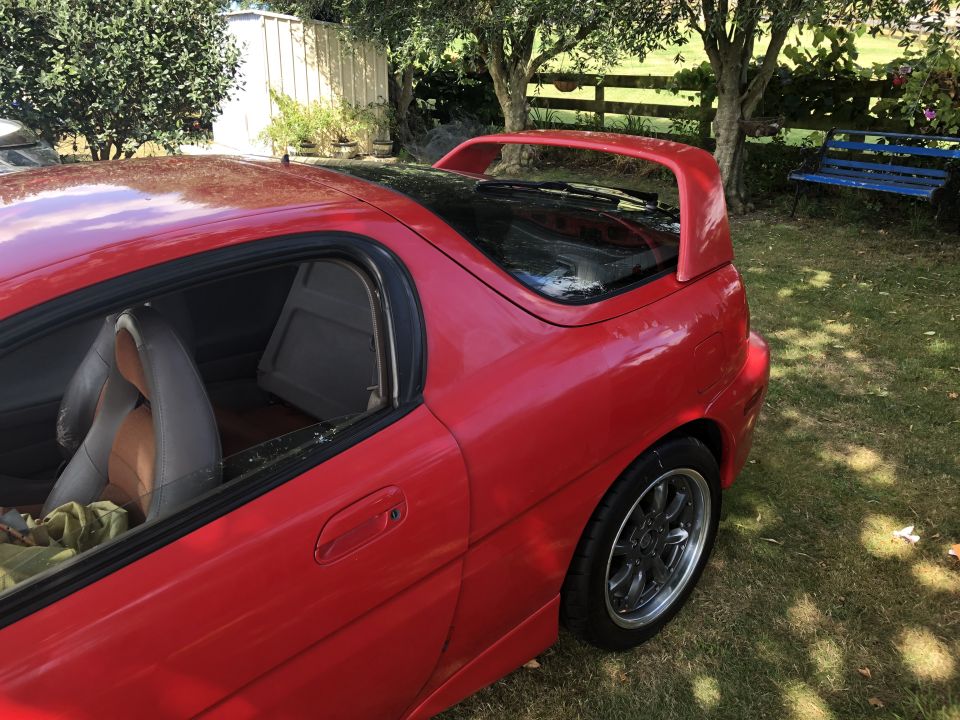 Red 1993 Mazda MX-3 coupe parked on grass, showing the right side profile.