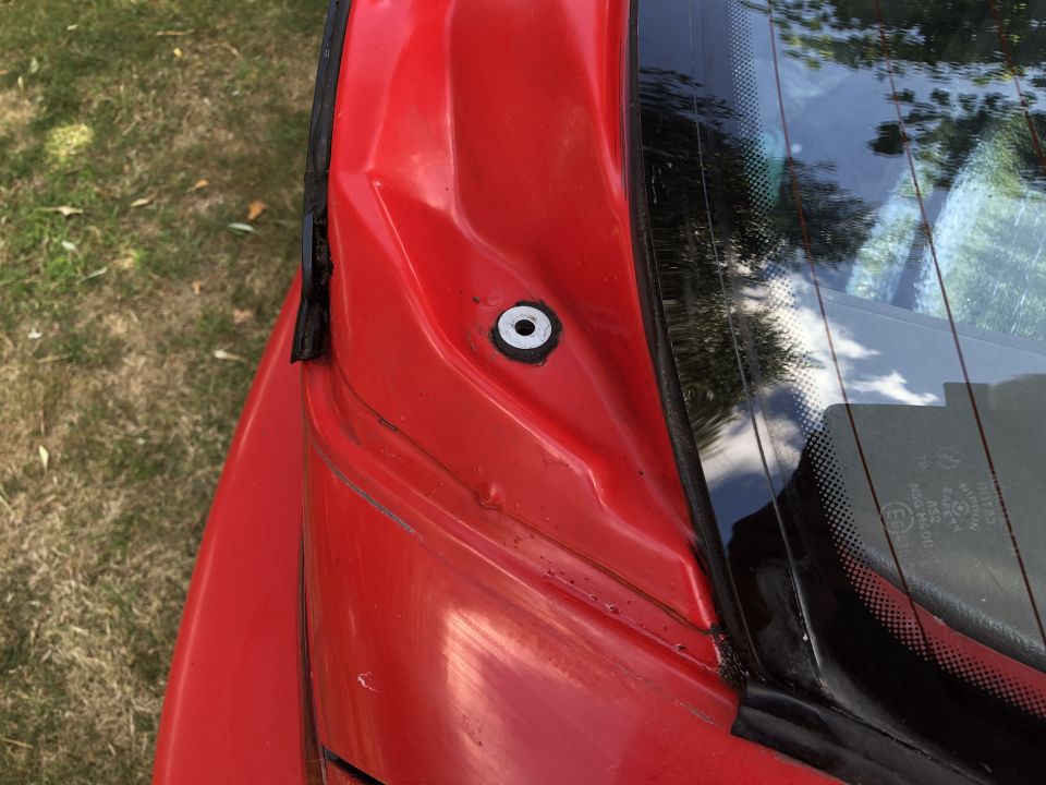Red car rear spoiler mounting point with visible dent and black trim near the rear window