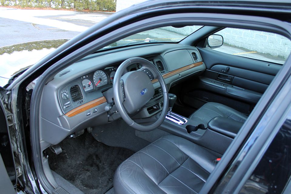 Black leather Ford sedan interior with woodgrain trim, column shifter and analog gauges