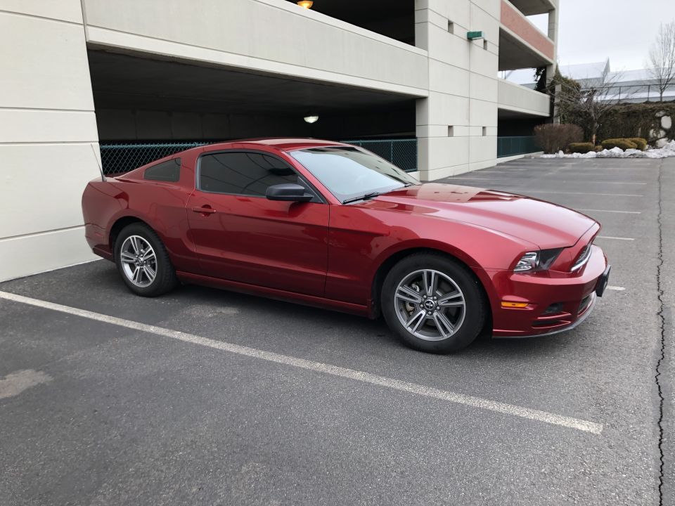 Red 2014 Ford Mustang coupe parked in a lot next to a parking garage