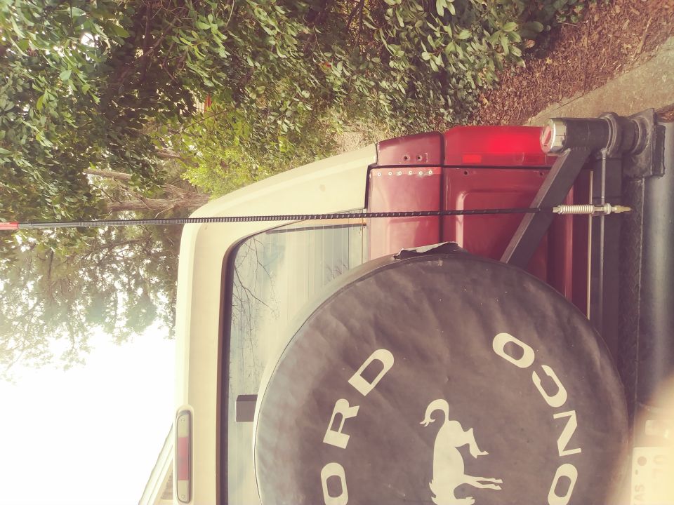 Rear of a beige and red Ford Bronco with a spare tire cover reading 'Ford Bronco' and a horse graphic