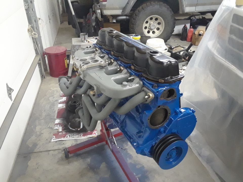 Blue engine block with grey intake manifold and exhaust headers on a red engine stand