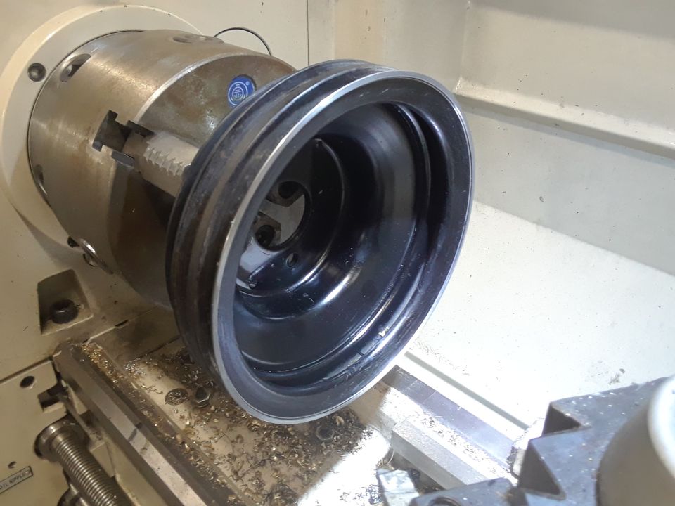 Crankshaft pulley held in a lathe chuck, metal shavings on the machine bed
