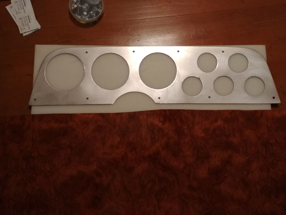 Custom aluminum panel with multiple circular cutouts for gauges, placed on wood grain surface