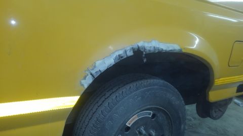 1996 Ford Bronco - The rear wheel well of a yellow vehicle has rust damage and is being prepped for repair.