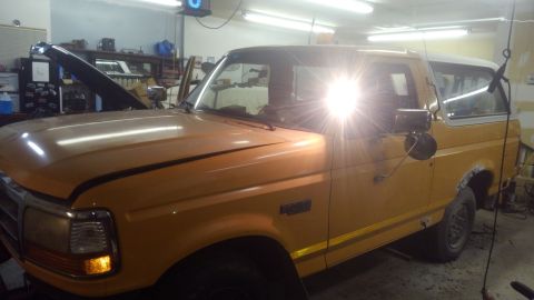 1996 Ford Bronco - A yellow Ford Bronco is parked in a garage with its hood open, showing a 3/4 front view.