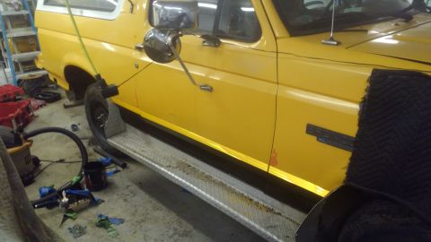 1996 Ford Bronco - Side view of a yellow 1996 Ford Bronco, showing its running boards and part of the interior.