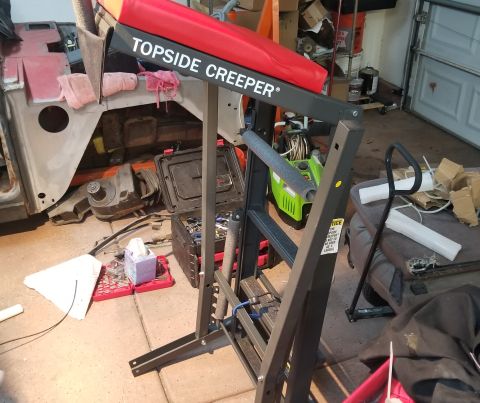 1993 Ford Bronco - A mechanic's creeper tool is positioned near vehicle components and tools in a garage setting.