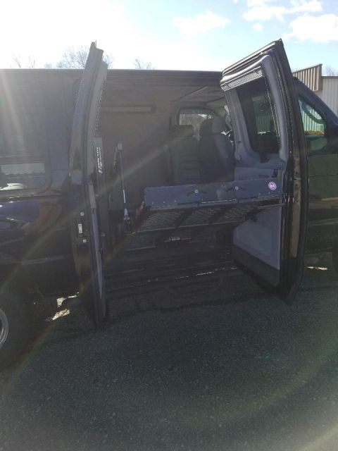 2010 Ford E250 - Side view of a dark van with passenger doors open, revealing a wheelchair lift inside.