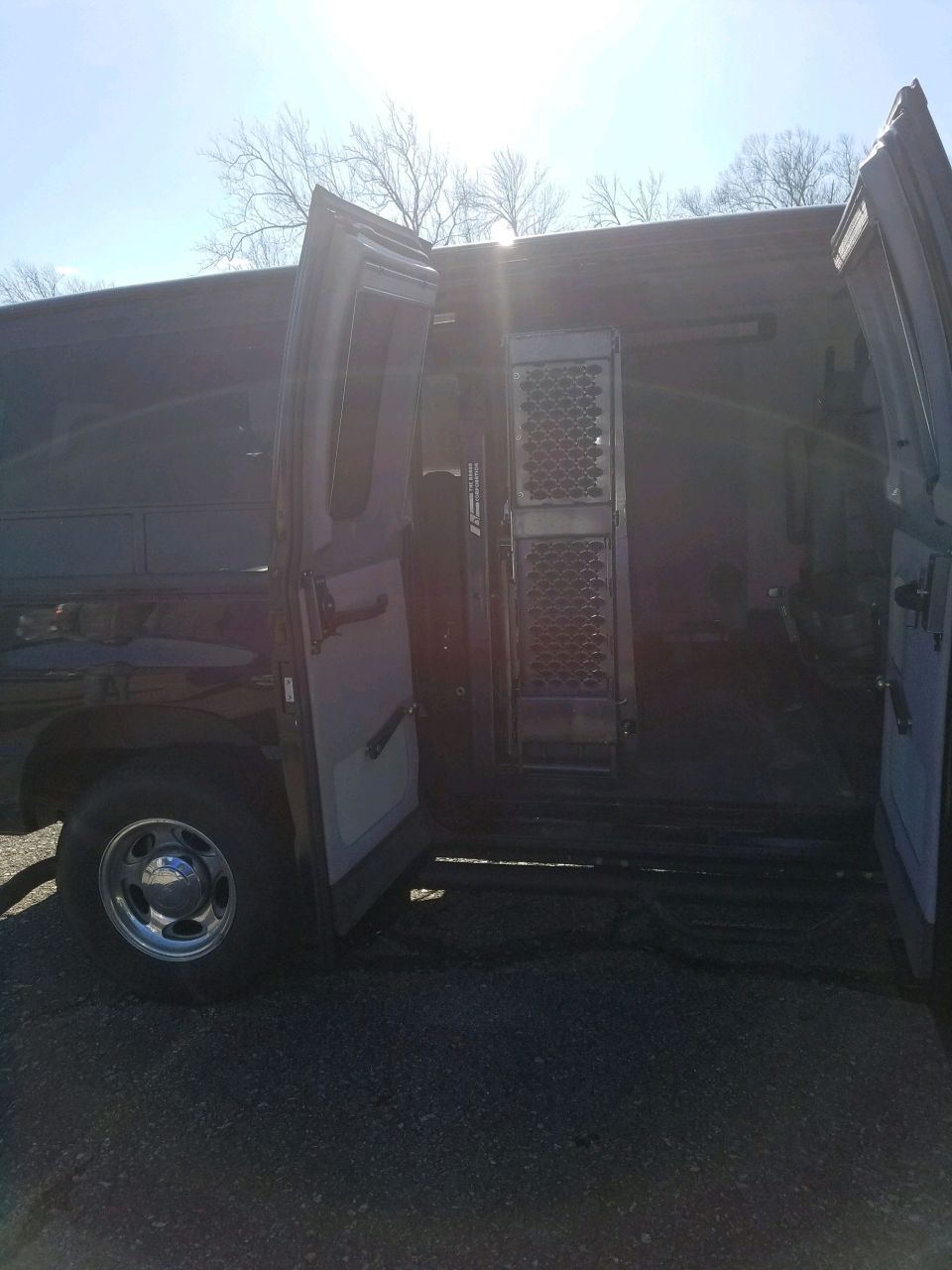 Dark-colored 2010 Ford E250 van with side doors and rear cargo doors open, showing interior metal grating