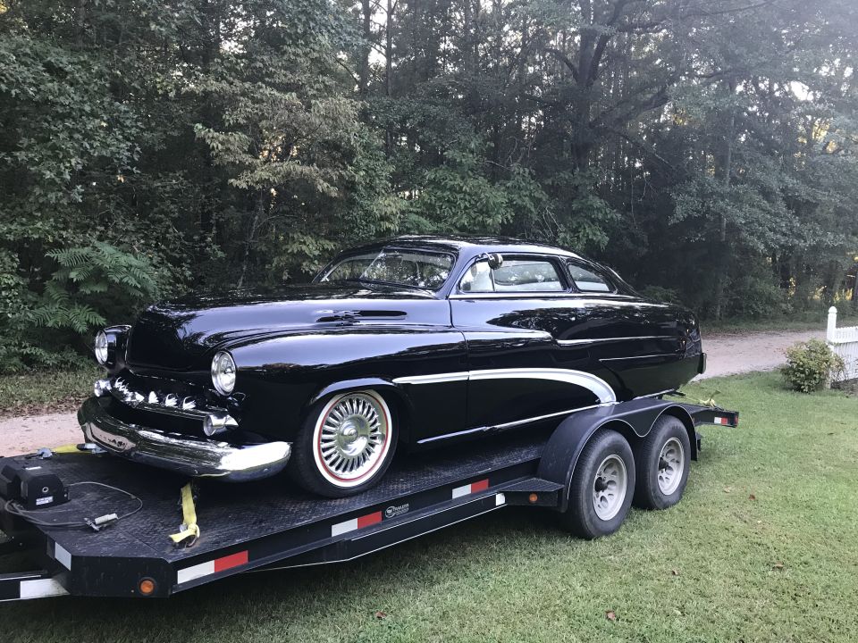 Black 1951 Mercury Sedan on a trailer, viewed from the front 3/4 angle, with chrome accents and whitewall tires