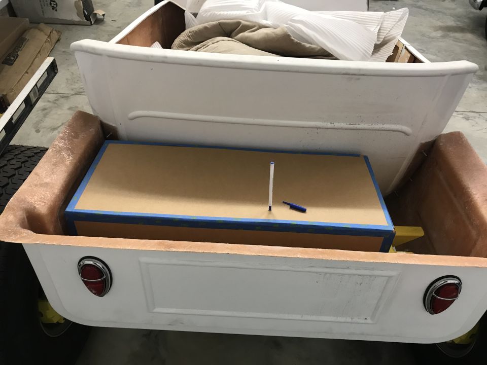Rear of a white pickup truck bed, carrying a large wooden box and other items. Tail lights visible